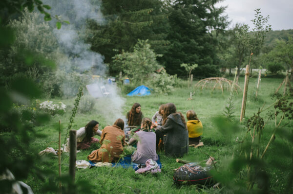 Frauen sitzen im Kreis auf Sommerwiese und entzünden ein Feuer. fotografiert von Tatyana Kronbichler